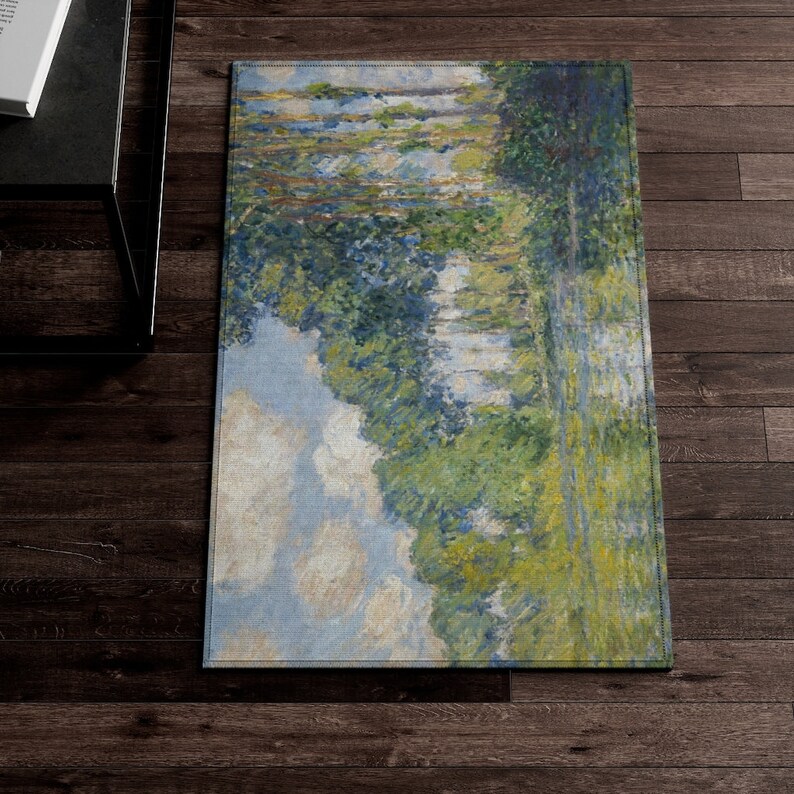 May include: A rectangular rug with a painting of a river scene. The painting features a blue sky with white clouds, green trees, and a river flowing through the center. The rug has a light blue background and a white border.