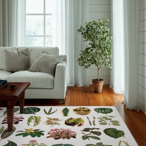 May include: A white rug with a botanical print featuring various green leaves and flowers. The rug is in a living room setting with a white sofa and a potted plant.