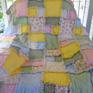 May include: A patchwork quilt with a variety of fabrics in pastel colors. The quilt features squares of pink, yellow, green, and blue fabrics, some with floral or striped patterns. The edges of the squares are frayed.