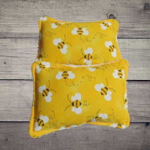 May include: Two yellow fabric pillows with a bee pattern. The pillows are stacked on top of each other.