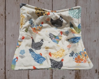 May include: A white quilted hot pad with a colorful chicken pattern. The chickens are in various poses and have different patterns on their feathers. The hot pad is square and has a white border.