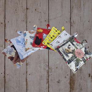 May include: A collection of six square fabric pot holders arranged in a fan shape. Each pot holder features a different pattern with chicken and rooster motifs in various colors including red, yellow, blue, black, white, and brown, each with a fabric loop.