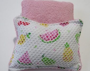 May include: A pink and white bath sponge with a mesh outer layer and a soft terry cloth inner layer. The sponge is decorated with a pattern of watermelons, pineapples, and pears.