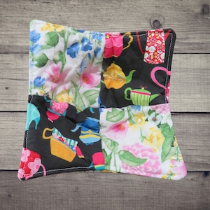 May include: A colorful patchwork pot holder with a floral design and teapots. The pot holder is made of fabric and has a quilted texture.