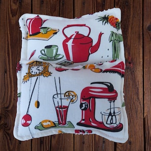 May include: A white, rectangular kitchen-themed pillow with a red teapot, mixer, and clock design. The pillow features a variety of kitchen-related illustrations in red, green, and yellow, with a cream-colored border.