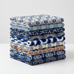 May include: A stack of folded fabric squares featuring various patterns in shades of blue, white, and orange. The designs include floral motifs, geometric shapes, botanical leaves, coral-like branches, and elephant silhouettes on the bottom layer.