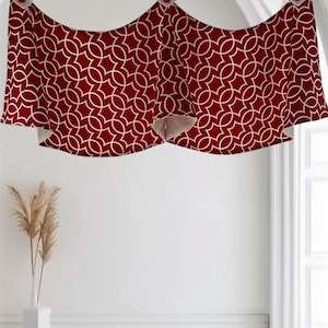 May include: A decorative valance with a geometric white pattern on a deep red background. The valance is suspended from a black rod with white fabric loops and red button accents. The design adds a touch of elegance to any window.