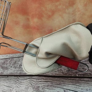 May include: A white leather grilling glove with a red handle and a metal grilling rack.