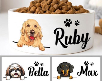 Può includere: Tre ciotole in ceramica bianca per cani con impronte di zampe e nomi. Le ciotole presentano illustrazioni di un golden retriever, uno shih tzu e un bassotto. I nomi sulle ciotole sono Ruby, Bella e Max.