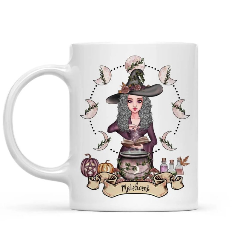 Puede incluir: Taza de cer&aacute;mica blanca con una ilustraci&oacute;n colorida de una bruja revolviendo un caldero. La bruja lleva un vestido morado y un sombrero negro con un dise&ntilde;o floral verde. La ilustraci&oacute;n est&aacute; rodeada de un c&iacute;rculo de lunas y el texto "Maleficent".