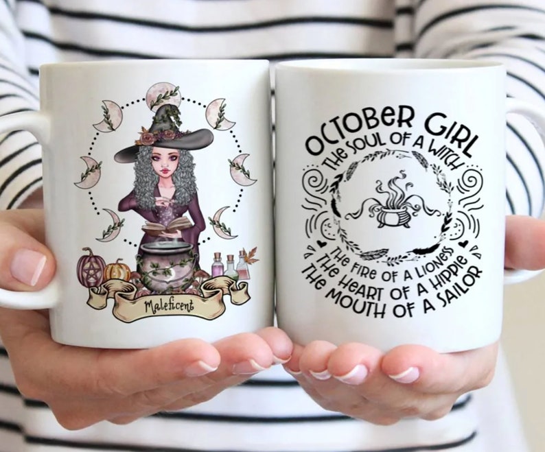 Puede incluir: Dos tazas de cer&aacute;mica blanca con texto negro e ilustraciones. Una taza presenta una bruja con un caldero y el texto "Maleficent". La otra taza presenta un caldero con el texto "OCTOBER GIRL THE SOUL OF A WITCH THE FIRE OF A LIONESS THE HEART OF A HIPPIER THE MOUTH OF A SAILOR".