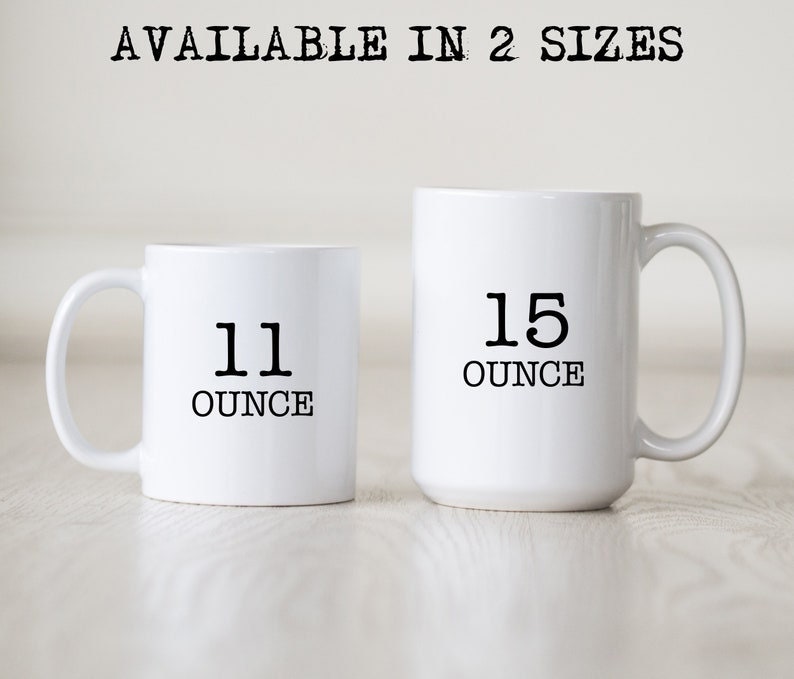 May include: Two white ceramic mugs, one smaller and one larger, with black text indicating sizes. The smaller mug reads "11 OUNCE" and the larger mug reads "15 OUNCE". The text "AVAILABLE IN 2 SIZES" is printed above the mugs.
