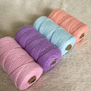 May include: Four spools of cotton rope in pastel colours: pink, purple, light blue, and peach. The spools are arranged in a row, with the pink spool at the bottom and the peach spool at the top.