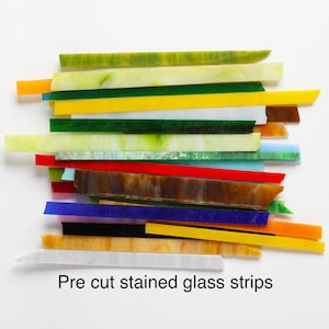 May include: Assortment of pre-cut stained glass strips in various colours, including green, yellow, red, blue, brown, and white. The strips are arranged in a random order and are ready for use in stained glass projects.