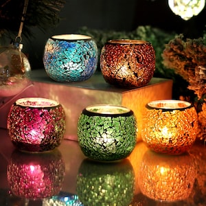 May include: Five tealight candle holders made of glass with a mosaic pattern. The candle holders are in different colours: blue, orange, green, purple, and gold. The candle holders are lit and casting a warm glow.