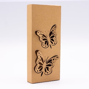 Puede incluir: Una caja de cartón marrón con dos recortes de mariposas. Las mariposas son negras con manchas blancas.