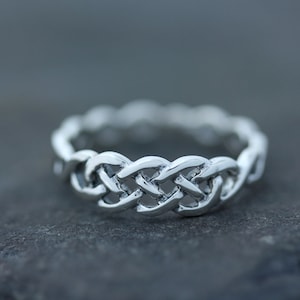 May include: A silver Celtic knot ring with a braided design. The ring is made of a smooth, polished metal and has a simple, elegant style.