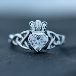 May include: A silver ring with a Celtic knot design and a heart-shaped clear stone set in a crown.