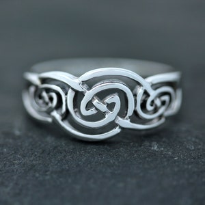 Puede incluir: Un anillo de plata con un diseño de nudo celta. El anillo está hecho de un metal liso y pulido y tiene un patrón intrincado de bucles entrelazados.