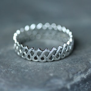 May include: A silver ring with a unique, intricate design featuring a repeating pattern of interlocking shapes.