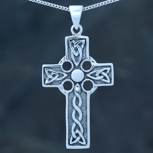 May include: A silver Celtic cross pendant with intricate knotwork designs. The cross has a circular center with four smaller circles around it.