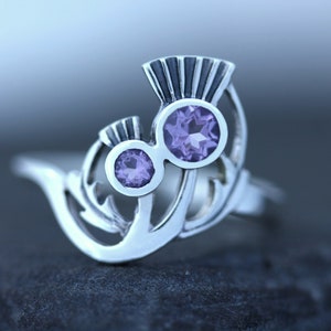 May include: Sterling silver ring featuring a stylized thistle design with two amethyst gemstones.