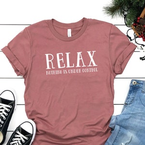 May include: A mauve t-shirt with the text "RELAX NOTHING IS UNDER CONTROL" in white lettering.