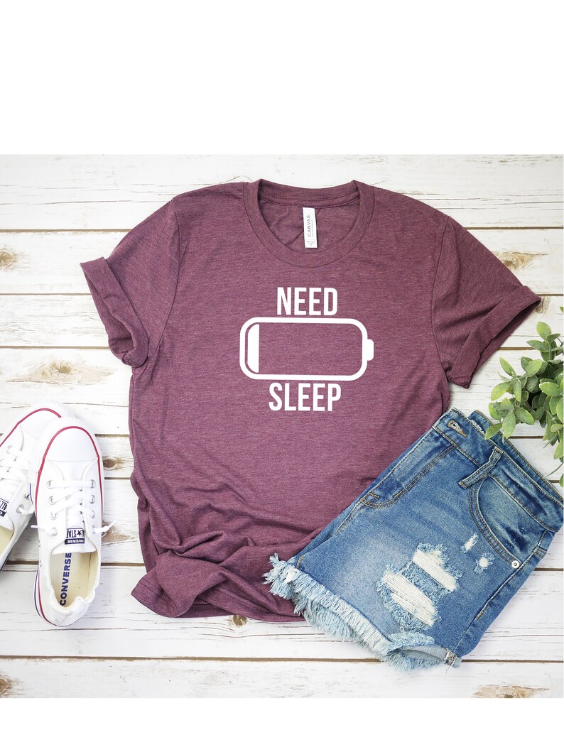 May include: A maroon t-shirt with the text "NEED SLEEP" and a white battery icon with a low battery level.