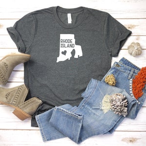 K&ouml;nnte beinhalten: Ein dunkelgraues T-Shirt mit einer wei&szlig;en Umrandung des Bundesstaates Rhode Island und dem Text "Rhode Island" mit einem kleinen Herzen innerhalb der Bundesstaatenumrandung.