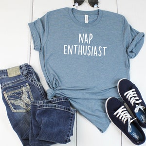 May include: A blue t-shirt with the text "NAP ENTHUSIAST" in white. The shirt is paired with blue jeans and blue sneakers.