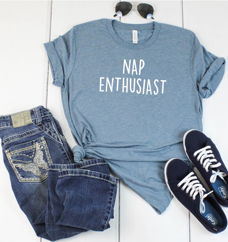 May include: A blue t-shirt with the text "NAP ENTHUSIAST" in white. The shirt is paired with blue jeans and blue sneakers.