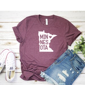 May include: A maroon t-shirt with a white outline of the state of Minnesota and the text "MINNESOTA" with a heart over the "A".
