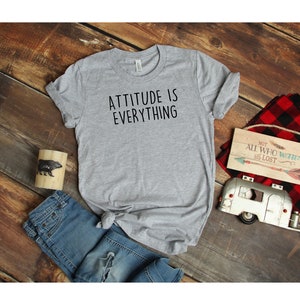 May include: Gray t-shirt with the text "ATTITUDE IS EVERYTHING" printed in black.
