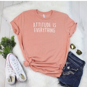 May include: A peach-colored t-shirt with the text "ATTITUDE IS EVERYTHING" printed in white on the front.