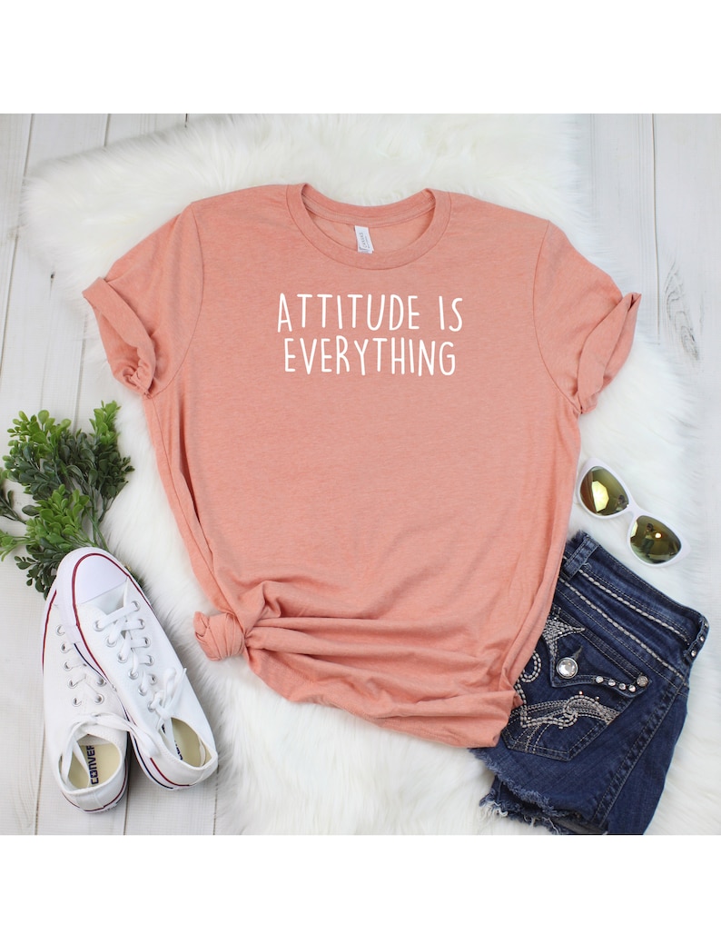 May include: A peach-colored t-shirt with the text "ATTITUDE IS EVERYTHING" printed in white on the front.