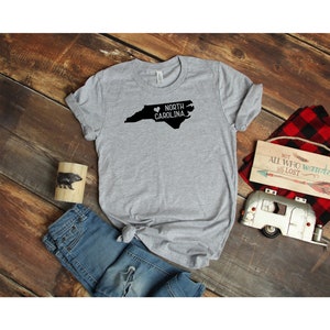 May include: A gray t-shirt with a black outline of the state of North Carolina and the text "North Carolina" with a heart symbol.