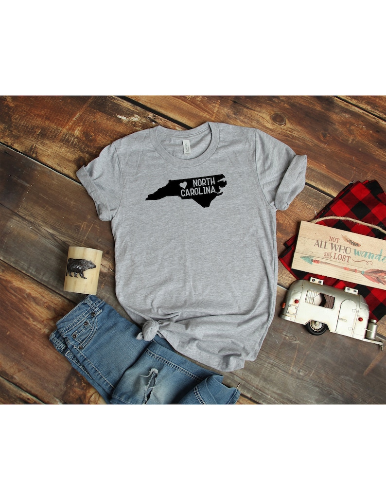 May include: A gray t-shirt with a black outline of the state of North Carolina and the text "North Carolina" with a heart symbol.
