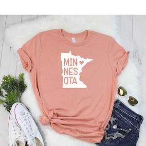 May include: A peach-colored t-shirt with a white graphic of the state of Minnesota with a heart in the middle and the text "MINNESOTA".