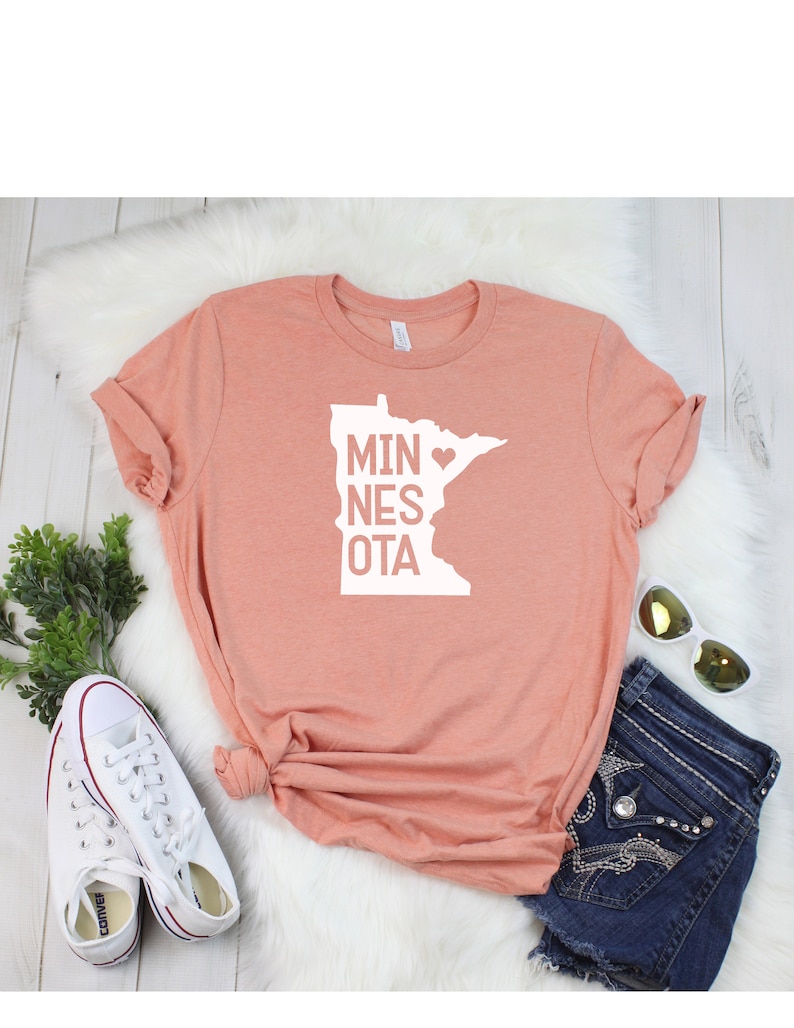 May include: A peach-colored t-shirt with a white graphic of the state of Minnesota with a heart in the middle and the text "MINNESOTA".
