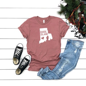 K&ouml;nnte beinhalten: Ein mauvefarbenes T-Shirt mit einer wei&szlig;en Umrandung des Bundesstaates Rhode Island und dem Text "Rhode Island" mit einem Herzen in der Mitte des Bundesstaates.