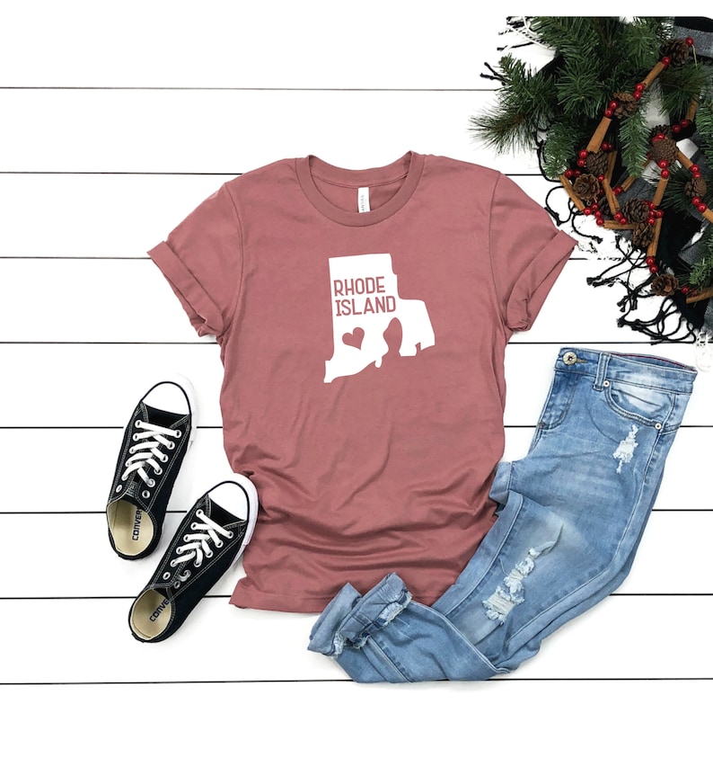 K&ouml;nnte beinhalten: Ein mauvefarbenes T-Shirt mit einer wei&szlig;en Umrandung des Bundesstaates Rhode Island und dem Text "Rhode Island" mit einem Herzen in der Mitte des Bundesstaates.