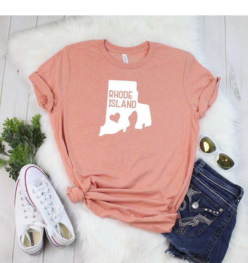 K&ouml;nnte beinhalten: Ein pfirsichfarbenes T-Shirt mit einer wei&szlig;en Umrandung des Bundesstaates Rhode Island und dem Text "Rhode Island" mit einem kleinen Herzen innerhalb der Bundesstaatenumrandung.