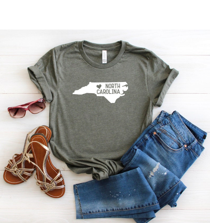 May include: A green t-shirt with a white outline of the state of North Carolina and the text "NORTH CAROLINA" with a heart in front of the word "NORTH".