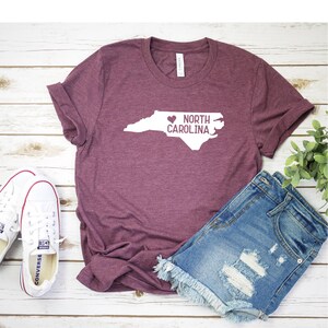 May include: A maroon t-shirt with a white outline of the state of North Carolina and the text "NORTH CAROLINA" with a heart in front of the word "NORTH".