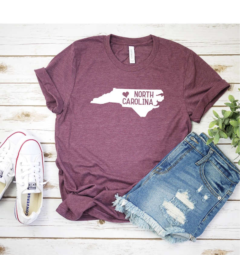 May include: A maroon t-shirt with a white outline of the state of North Carolina and the text "NORTH CAROLINA" with a heart in front of the word "NORTH".