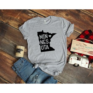 May include: Gray t-shirt with a black outline of the state of Minnesota and the text "MINNESOTA" with a heart in place of the "O".