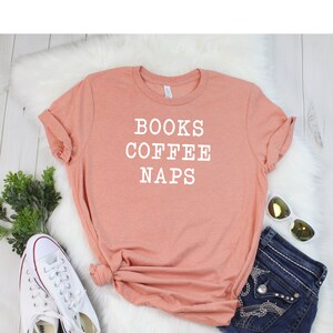 May include: A peach-colored t-shirt with the text "BOOKS COFFEE NAPS" printed in white.