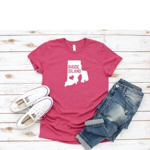 K&ouml;nnte beinhalten: Ein pinkfarbenes T-Shirt mit einer wei&szlig;en Umrandung des Bundesstaates Rhode Island und dem Text "Rhode Island" mit einem kleinen Herzen innerhalb der Bundesstaatenumrandung.