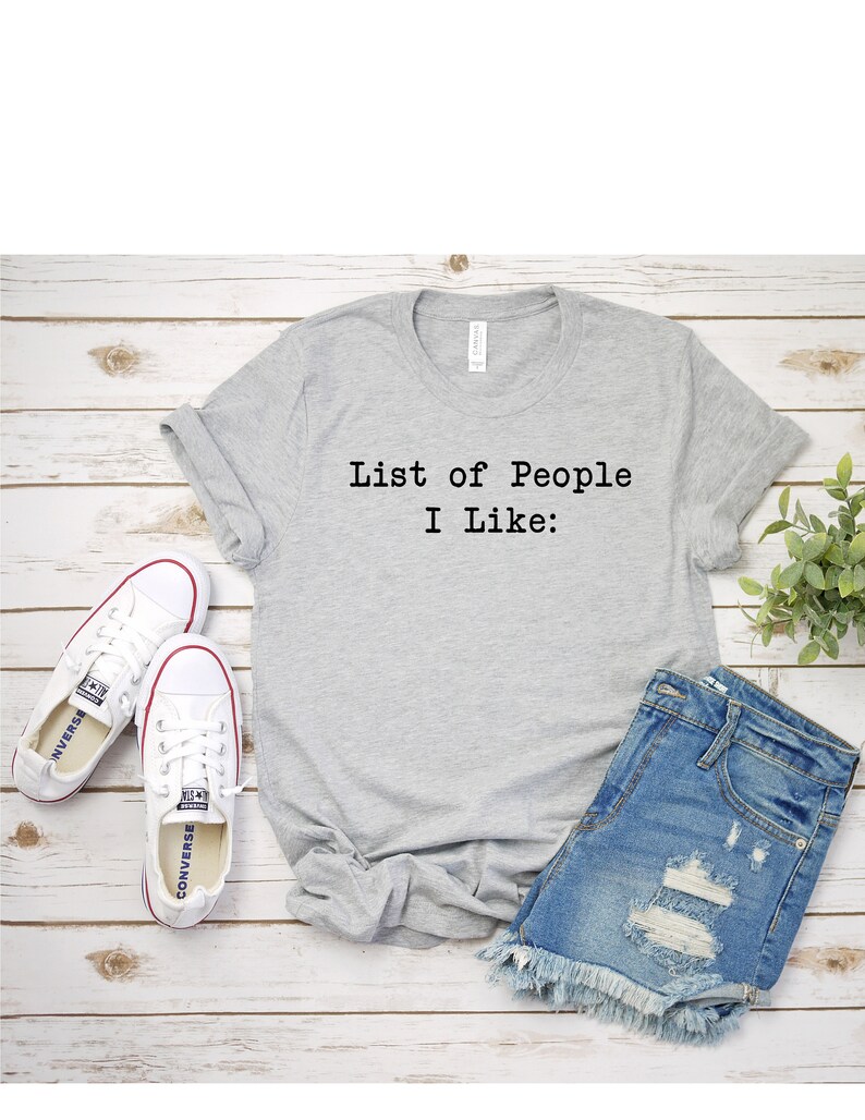 May include: A gray t-shirt with the text "List of People I Like:" printed on the front. The shirt is paired with denim shorts and white sneakers.