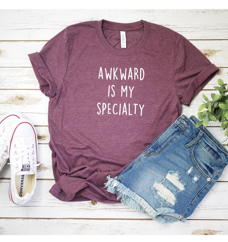 May include: A maroon t-shirt with the text "Awkward is my specialty" in white lettering.